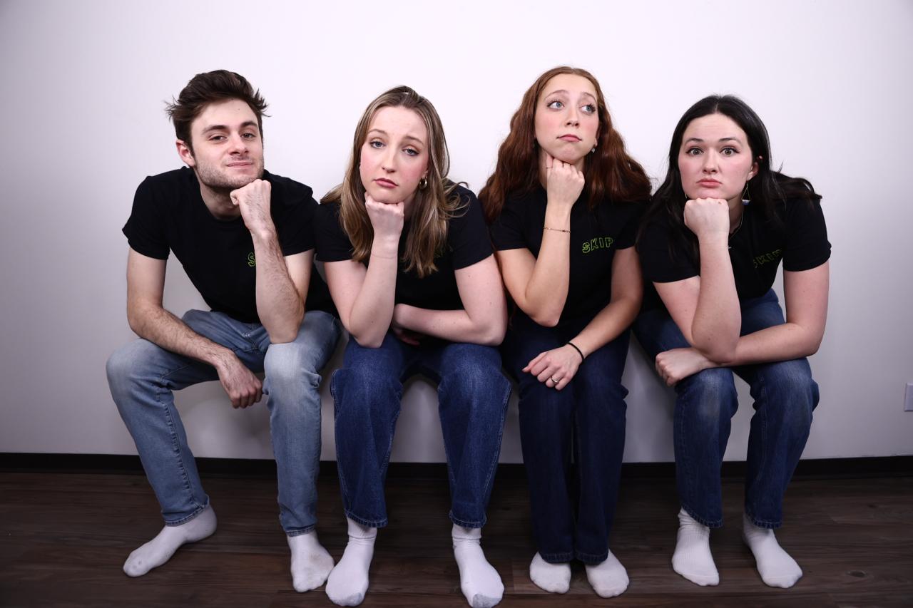 The four members of Skip Skip sitting in a row in matching SKIP tees, chins resting on fists